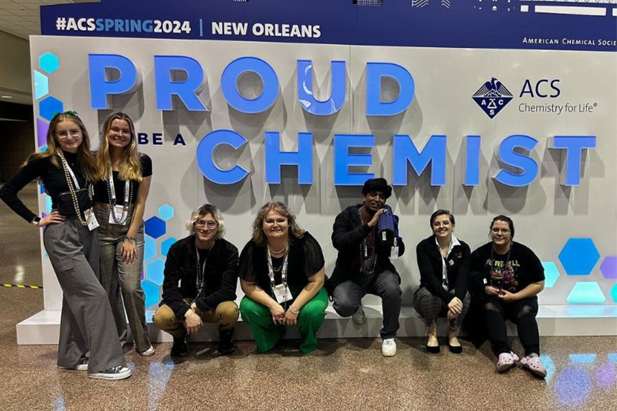 Seven members of the CMU student chapter of the American Chemical Society gather in front of a sign that reads, Proud Chemist at the 2024 convention in New Orleans.
