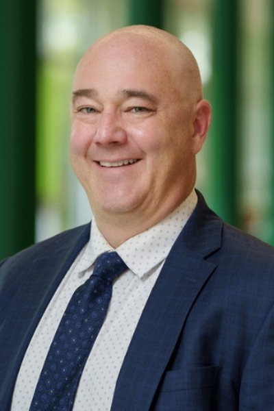A man in a suit smiling in a long hallway.