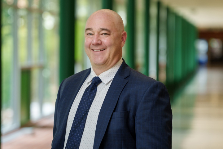 A man in a suit smiling in a long hallway.
