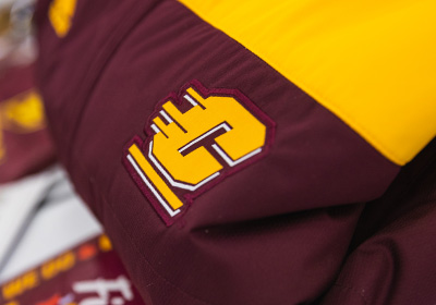 Central Michigan University's Action C in gold with white drop shadows, placed on a solid maroon jacket that is folded over on a table.