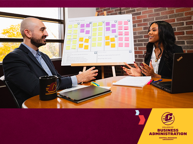 Two students in business attire sit at a conference table littered with pens papers and laptops. A poster board with color sticky notes is on an easel behind them. The College of Business Administration logo sits on a gold shape in the lower left corner.