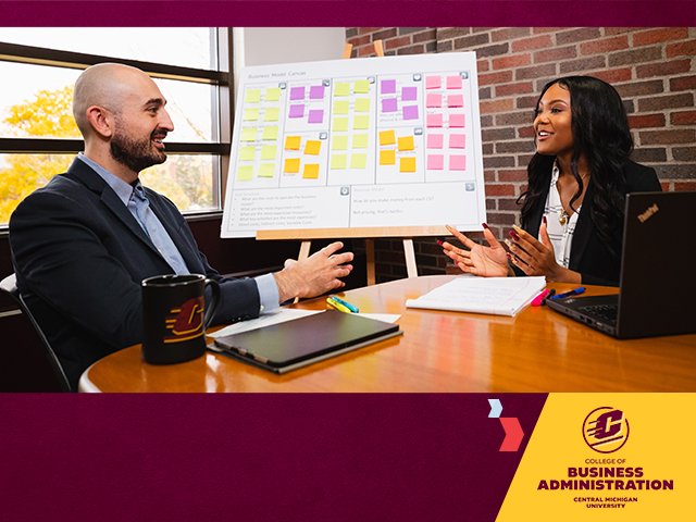 Two students in business attire sit at a conference table littered with pens papers and laptops. A poster board with color sticky notes is on an easel behind them. The College of Business Administration logo sits on a gold shape in the lower left corner.