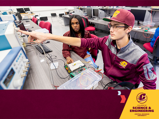 A dark-haired female student and a male wearing a maroon baseball cap and maroon zip-up sweater, work in an electrical engineering lab with wires and cables across the light grey desk. The Science and Engineering logo in the right corner on a gold shape.