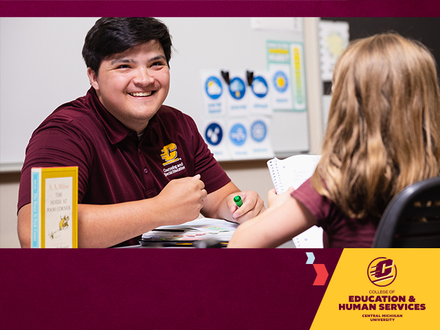 A male student teacher in a maroon polo with short black hair sits across from a blonde female middle school student in a classroom setting, the College of Education and Human Services logo in the low right on a gold shape, on a maroon background.
