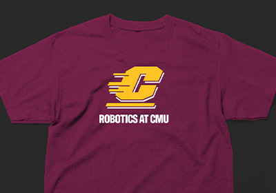A gold CMU Action C with a white drop shadow sits above the words "Robotics at CMU" in bold white all cap letters on a maroon shirt placed on a dark gray background.