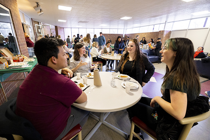 Four students sit around a table, talking and enjoying international cuisine.