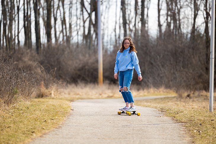 CMU Student, Hannah Ardelean longboards through the CMU Disc Golf Course