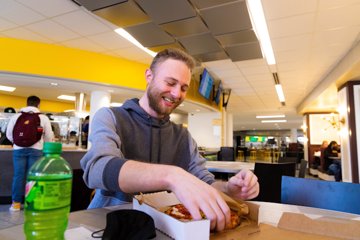 University Communications intern Michael Armistead preps for his first bite of his mozzarella, pepperoni, and banana pepper pizza at Build Pizza by Design in Central Eats inside the University Center.