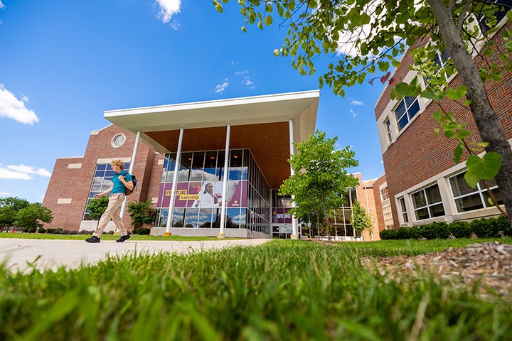 A student walks in front of the Health Professions Building on a summer afternoon.