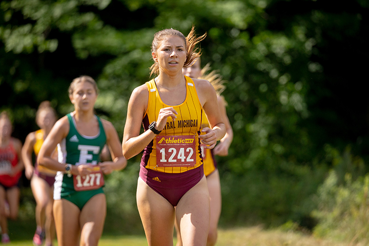 A female CMU cross country runner leads a group of runners during a race.