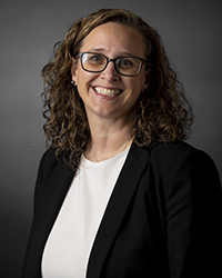 Erica Johnson wears a white shirt and black jacket, smiling at the camera in front of a gray background.