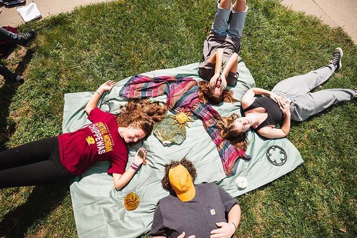Four students lie on the ground on top of a blanket.