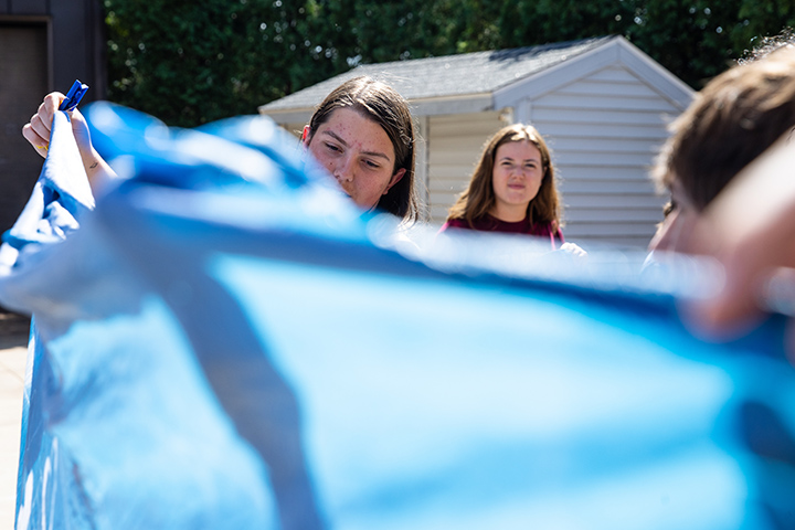 A faculty member holds a large blue blanket-type material while students look on.