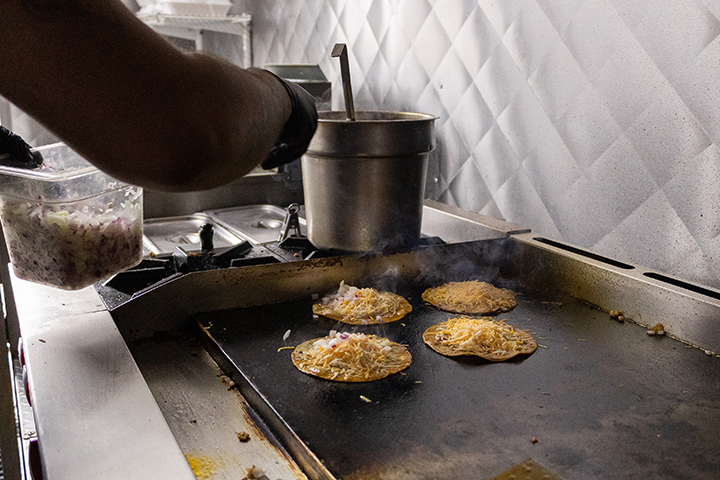A griddle sizzles while cooking food inside a food truck.