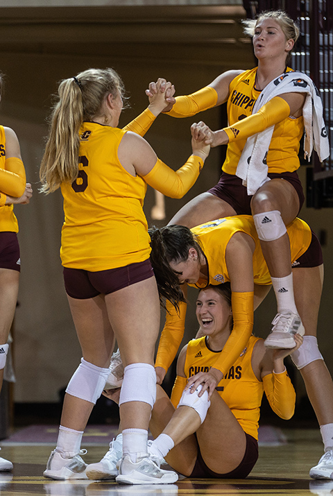 A group of CMU women's volleyball players climb on top of each other and joke around on the sidelines.
