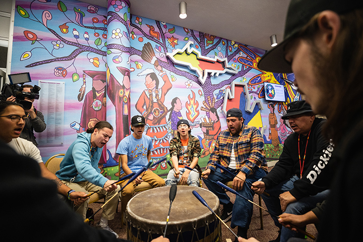 Eight men sit around a drum performing during the Native American mural dedication ceremony.