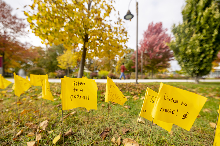Small, yellow flags with encouraging words written on them stick out of the ground near Warriner Hall.