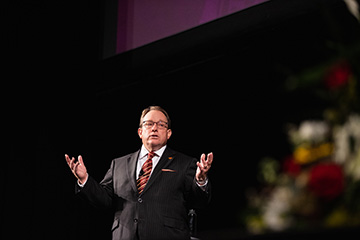 CMU President Bob Davies addresses the crowd while standing on stage at Plachta Auditorium.
