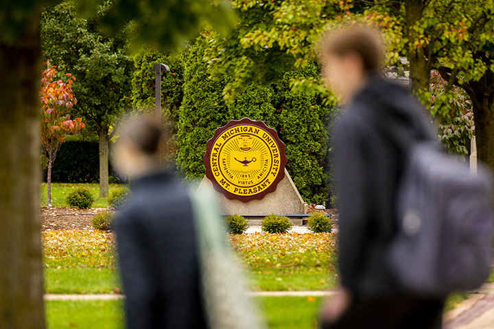 The CMU seal centered in the picture with two out of focus students walking in the foreground.