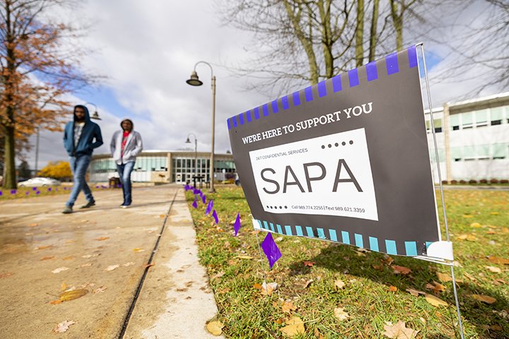 Two students walk down the sidewalk past a sign that reads 