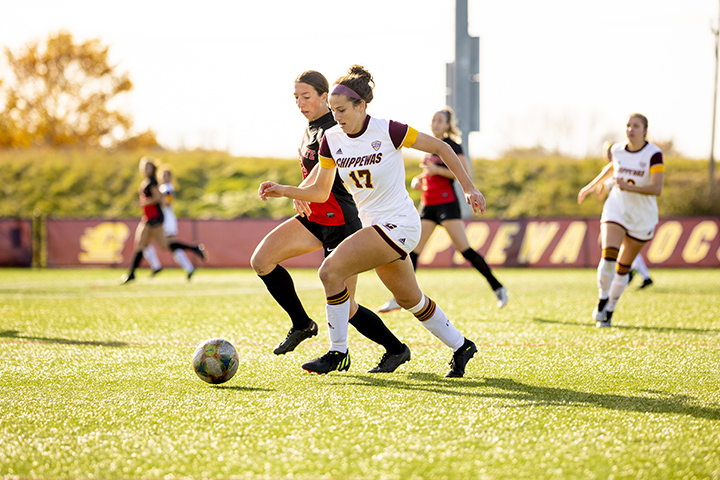 Two female soccer players battle for a soccer ball on a soccer field.