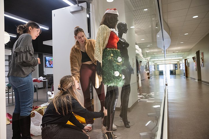 Three students arrange mannequins in a display window.