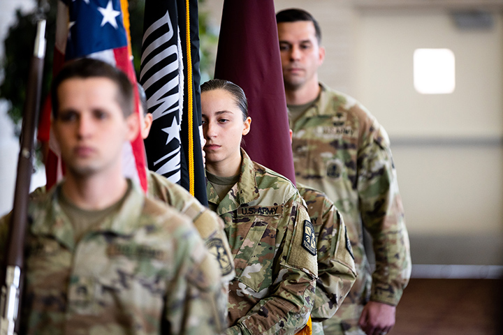 Three members of the Army ROTC program stand at attention with flags.