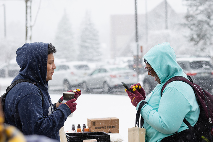 Two students in hoodies enjoy soup on a snowy day.