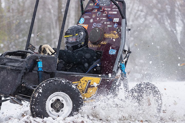 A Baja race car with a CMU logo on its side door races through the snow.