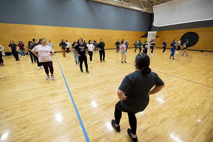 A large group of students learn Pow wow dance styles from an instructor.
