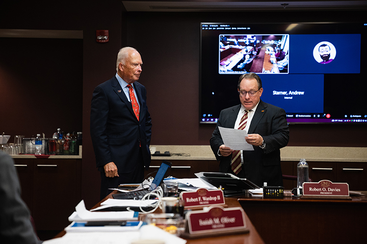 President Bob Davies and Board of Trustees member Robert F. Wardrop II stand next to a table while President Davies reads from a piece of paper.