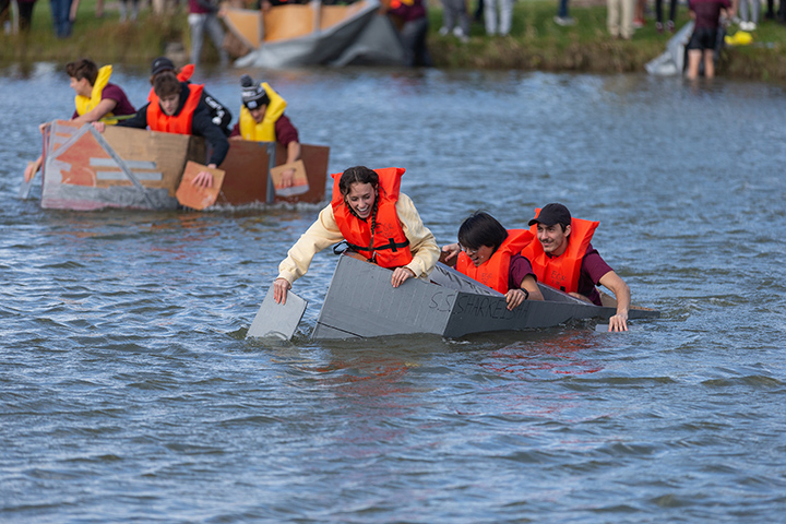 Two teams of three people riding in cardboard canoes try to stay afloat in Rose Pond.