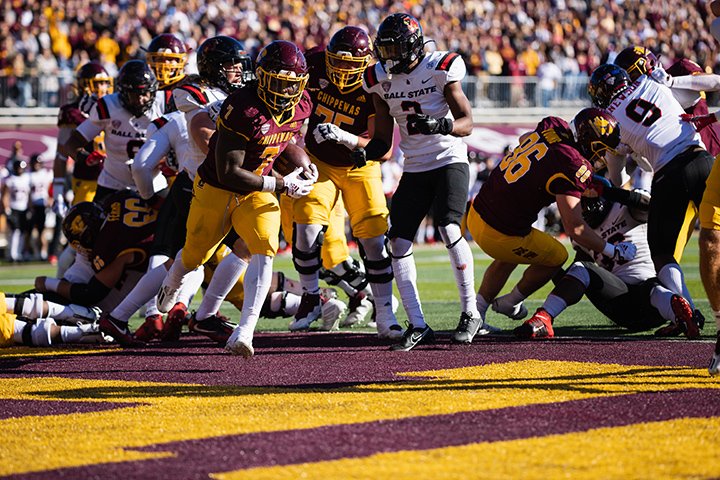 A CMU football player carries the football through a group of Ball State players.