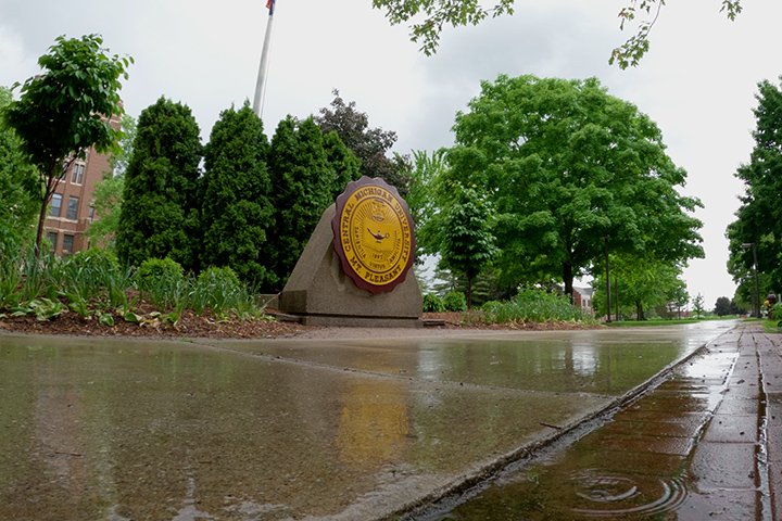 Rain falls on the sidewalk in front of the CMU seal near Warriner Hall.