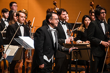 Jose-Luis Maurtua stands alongside an orchestra.