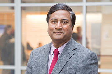 Dr. Sethu K Reddy smiles at the camera while wearing a gray suit coat and red tie.
