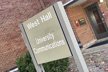 A sign outside a brick building reads West Hall University Communications.