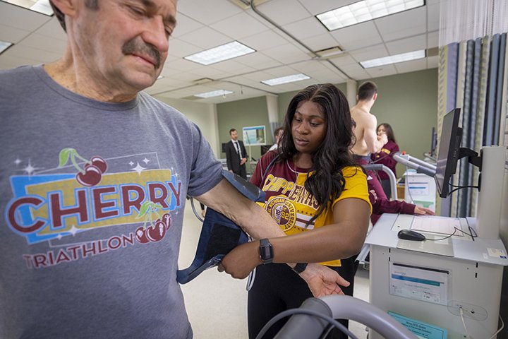 An exercise science student puts a blood pressure arm cuff on a patient.