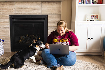 Woman works on laptop at home with dog.