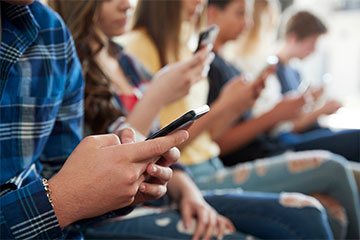 Students seated in a row looking at their cellphones