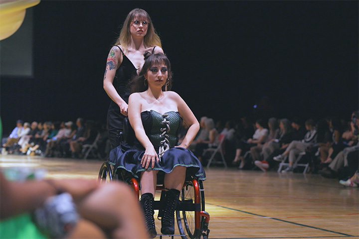A woman in a wheelchair is pushed down the runway during the Threads Fashion Show.