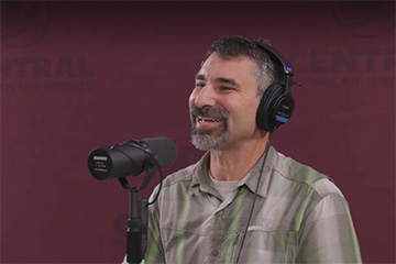 Central Michigan University philosophy faculty member Matt Katz wearing headphones sitting in front of a microphone to record a new podcast episode.