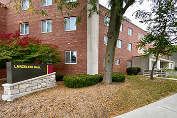 A red brick building surrounded by fall foliage and a sign that reads Larzelere Hall.