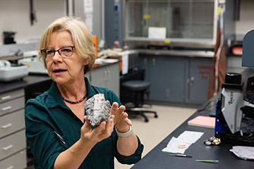 Monalisa Sirbescu, a woman with blonde hair and glasses, wearing a teal blouse, holds a piece of rock with lithium in it.