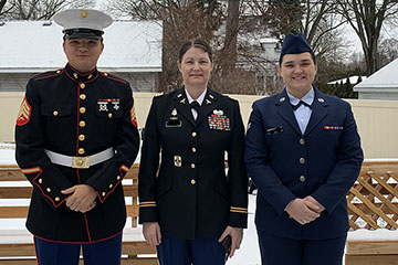 A man in Marine dress blues stands nexts to a woman in an Army officer's uniform and a woman in an Air Force uniform.