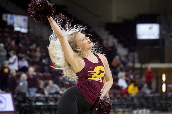 A blonde CMU dance team member in a maroon CMU shirt performs a dance on a basketball court.