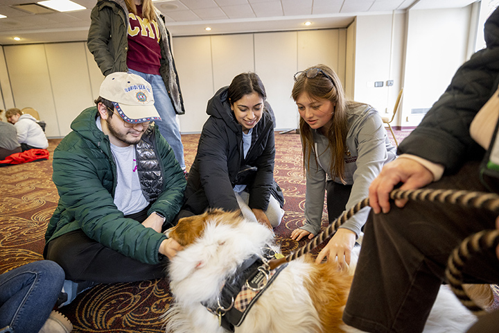 Three students pet a fluffy dog while sitting on the floor inside the Bovee University Center.