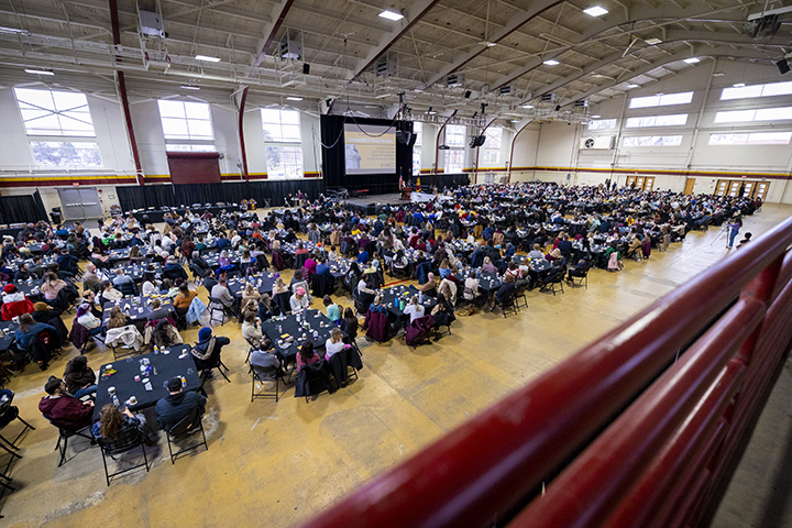 Hundreds of people sit at tables inside Finch Fieldhouse as a presenter speaks from a stage during the MLK Community Peace Brunch.