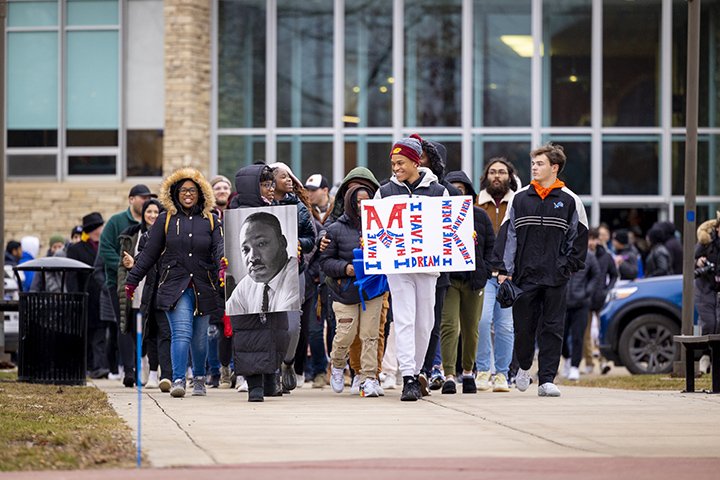 Hundreds of students march on a sidewalk carrying signs with Martin Luther King Jr.'s likeness and words from his
