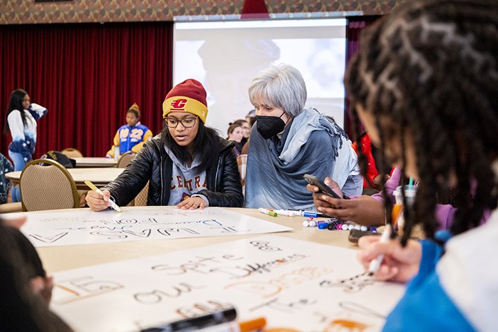 Students sit at a table creating signs and banners to be used in the MLB Community Peace March and Vigil.